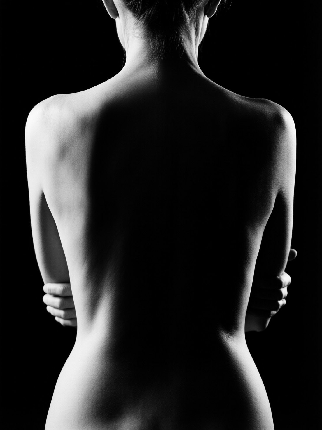 Dos de femme dans l'ombre, les bras croisés : la lumière ne dessine que le contour des épaules et de la taille